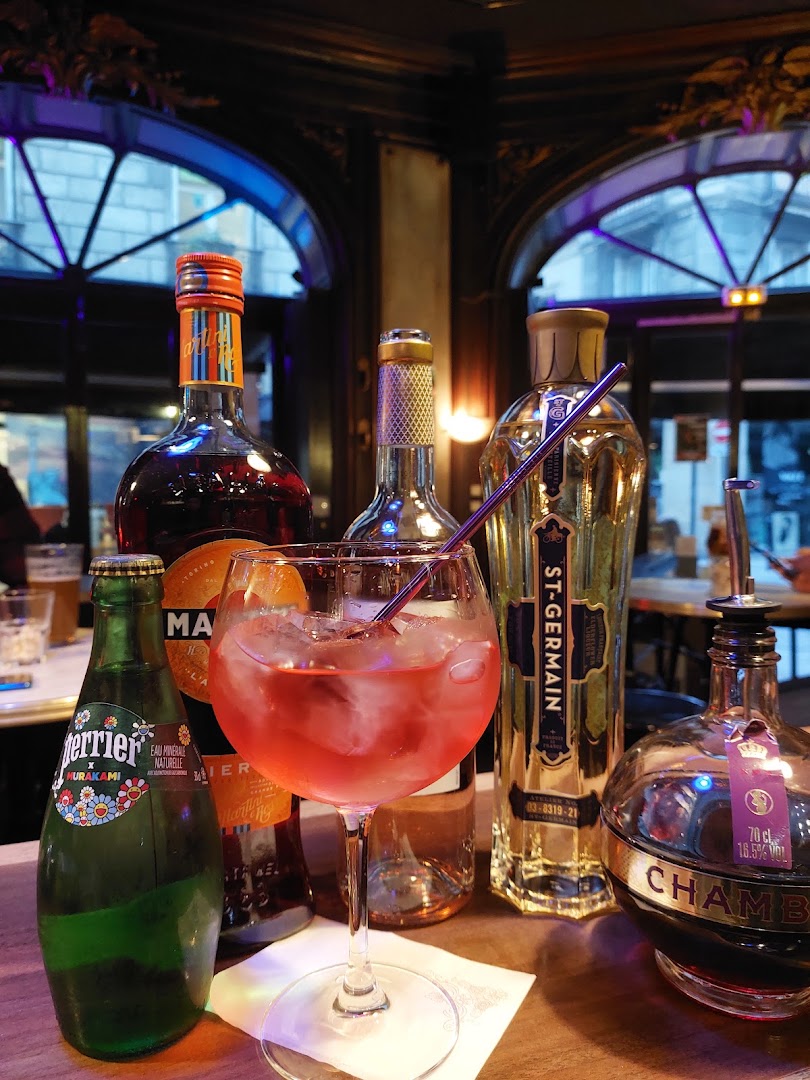Un cocktail rose entouré de bouteilles au bar
